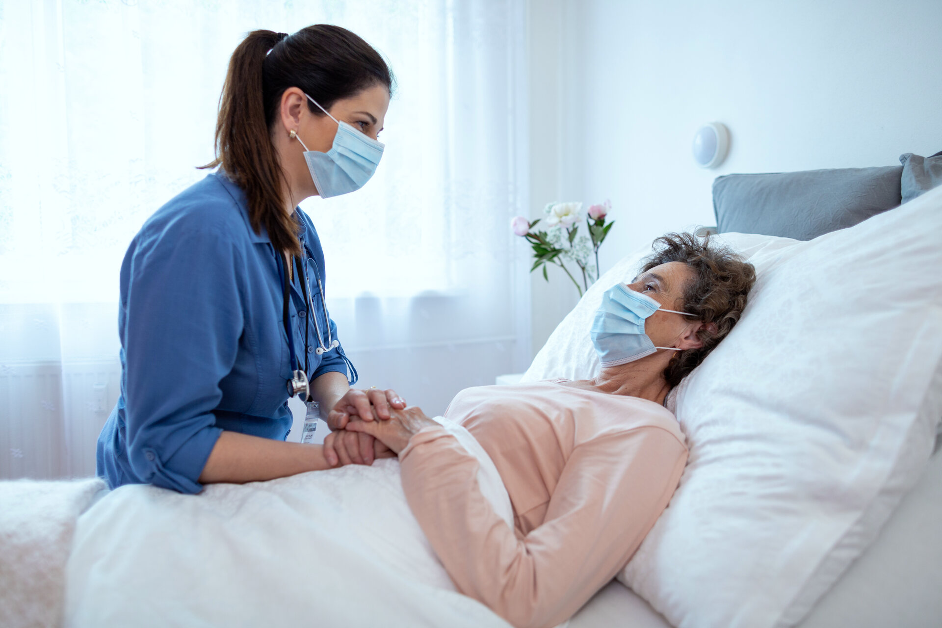 Nurse holding hand of elderly patient in bed providing compassionate hospice care
