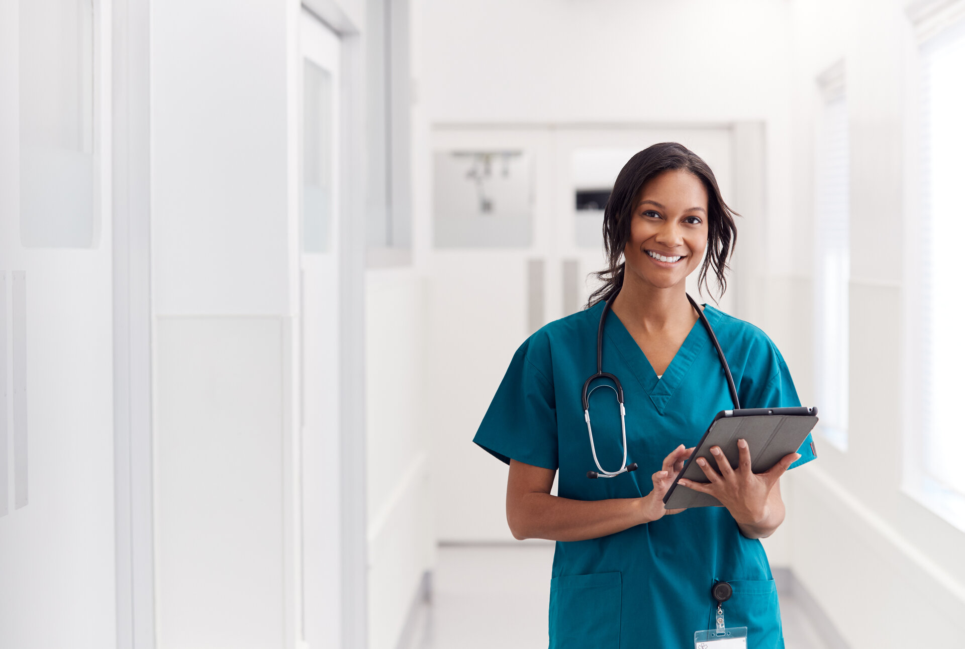 Smiling nurse with tablet in hospital corridor supporting acute care health system